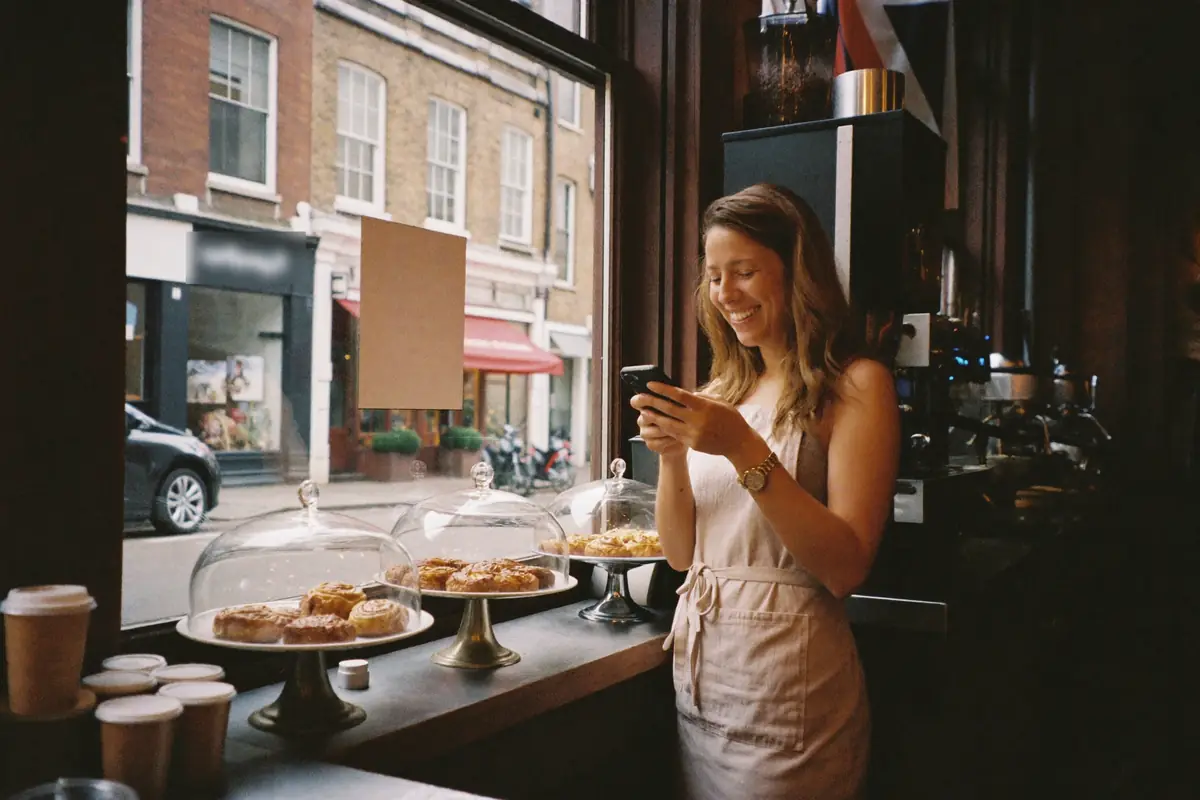 A café owner by her shop window, smiling at her phone